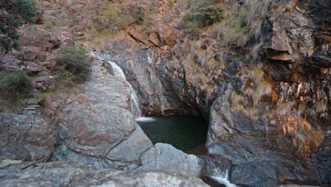 Secluded-waterfall-oasis-among-rugged-cliffs-at-dusk,-aerial-view