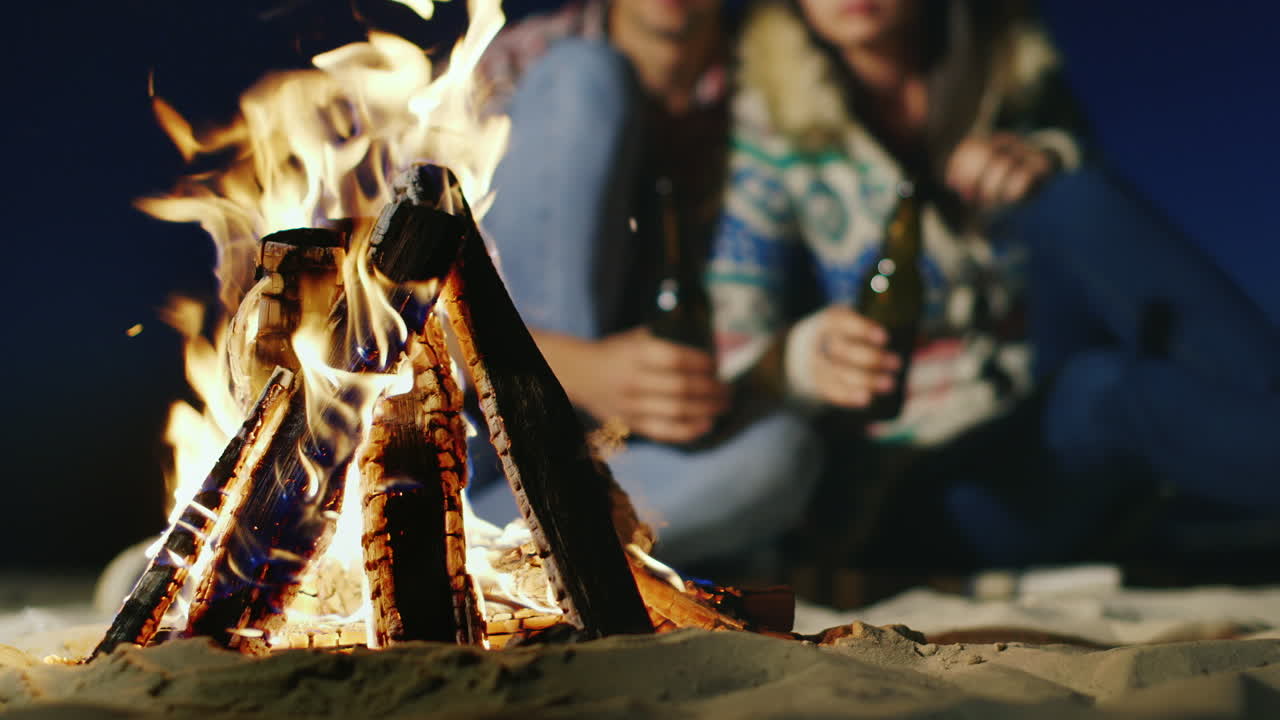 jóvenes relajándose junto al fuego en las manos sosteniendo una botella de cerveza o limonada el fuego en el