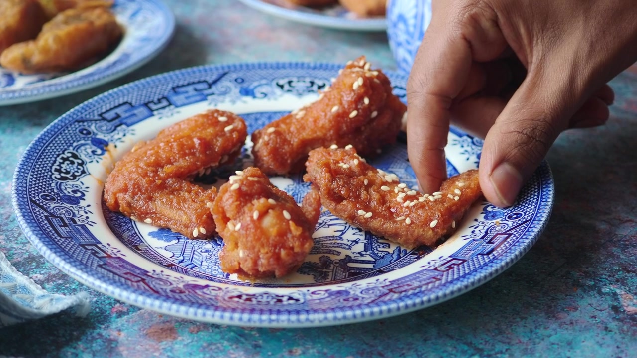 Hånd tager en sprød friteret kyllingevinge fra en dekorativ tallerken