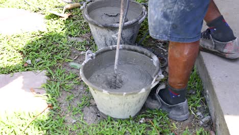worker mixes cement in buckets outdoors under bright sunlight. the scene captures manual labor and construction activity