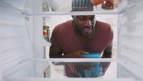 view looking out from inside of refrigerator as man stacks healthy packed lunches in containers