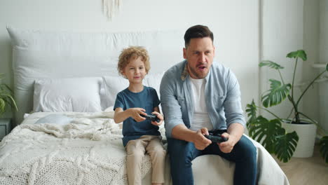 father and son playing video games together in bedroom