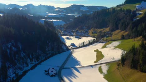 aerial drone footage of a small village in the emmental in the canton of bern, switzerland, showing small town buildings, and home and surrounding snowy mountains