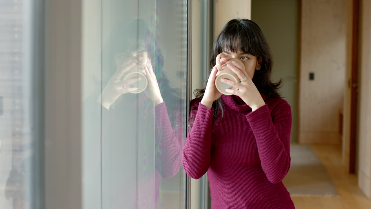Woman enjoying coffee by window at home, reflecting and relaxing indoors, copy space