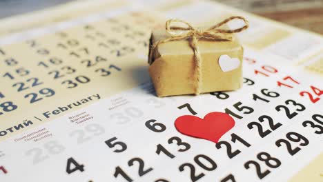 hand puts red paper heart on the number 14 on a calendar and small gift with a bow. love holiday