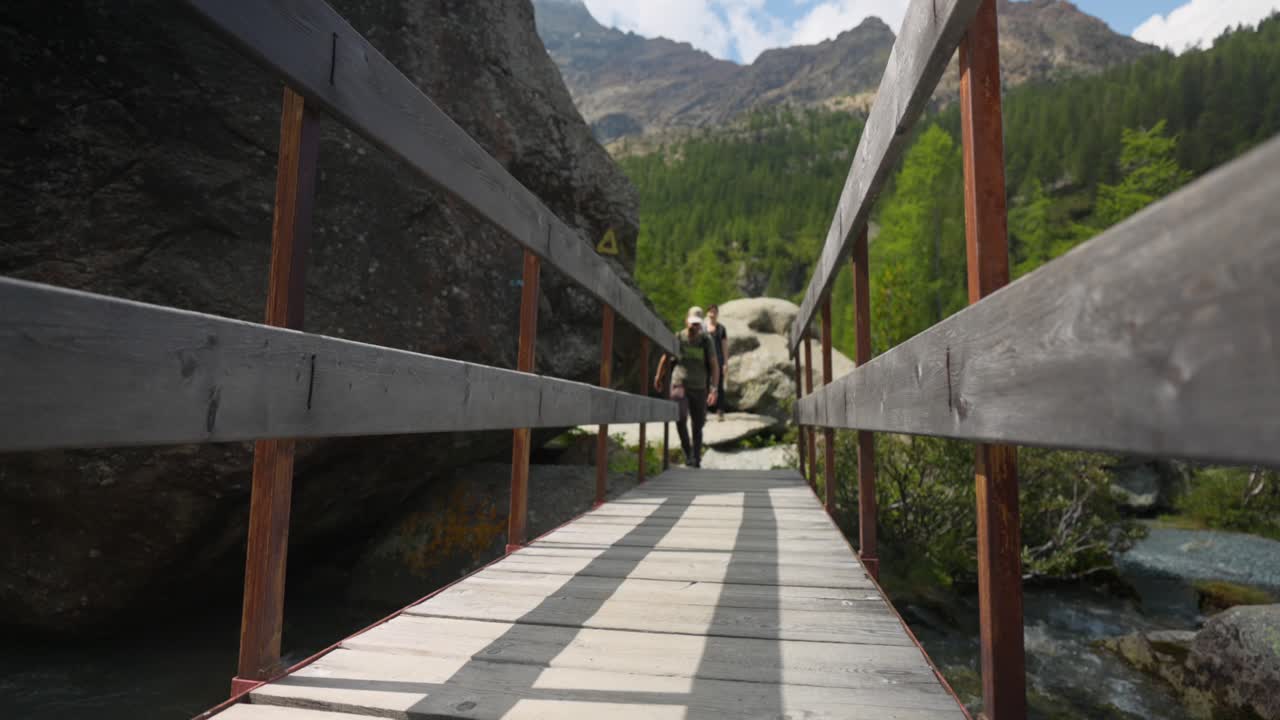 puente de madera con un hombre cruzando el arroyo del río de la montaña durante la caminata