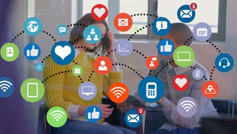 animation of network of digital icons over two diverse female colleagues discussing at office