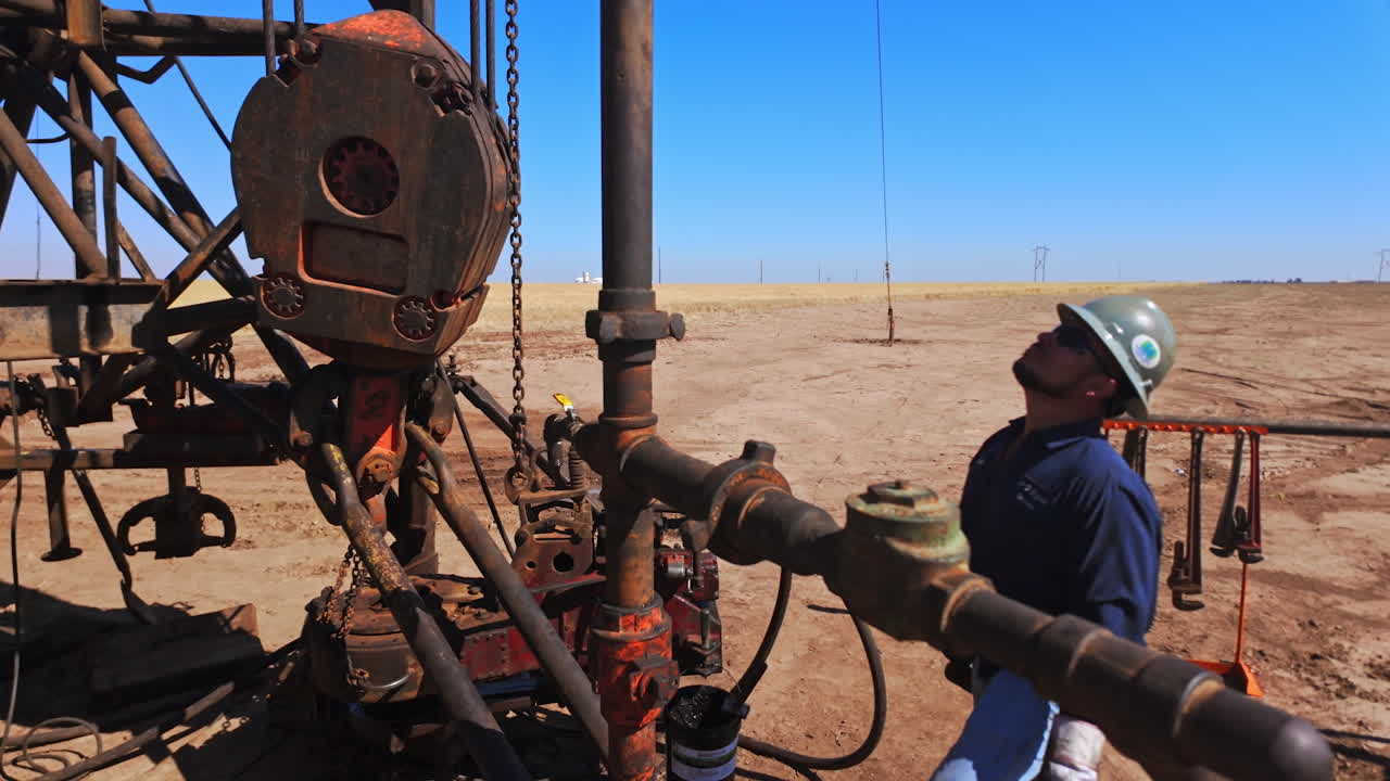 Uniformed men in protective helmets installing the equipment at the site for oil production. Industry for natural resources extraction.