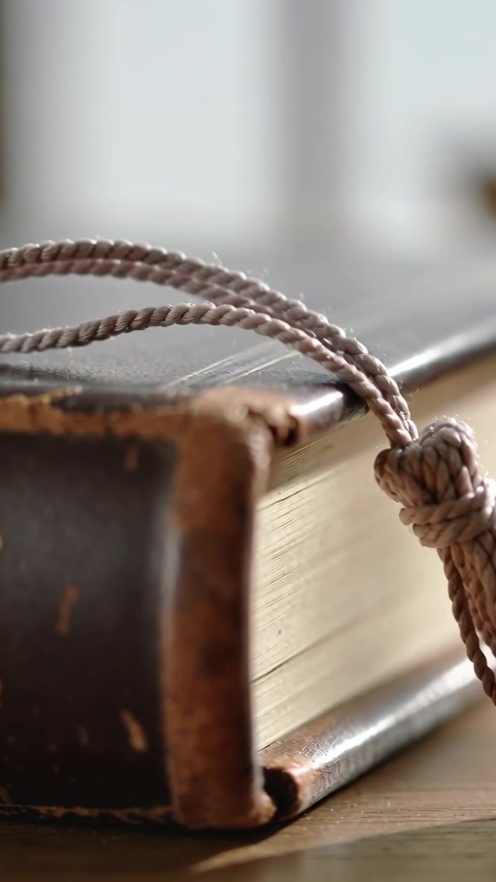 Video verticale: Telecamera che panoramica rivelando un libro di pelle usurato, un cordino intrecciato e una nappa su un tavolo di legno.