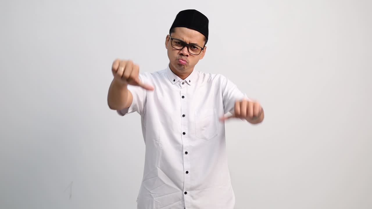 Aasialainen muslimimies, jolla on surullinen ilme, näyttää peukkua alaspäin