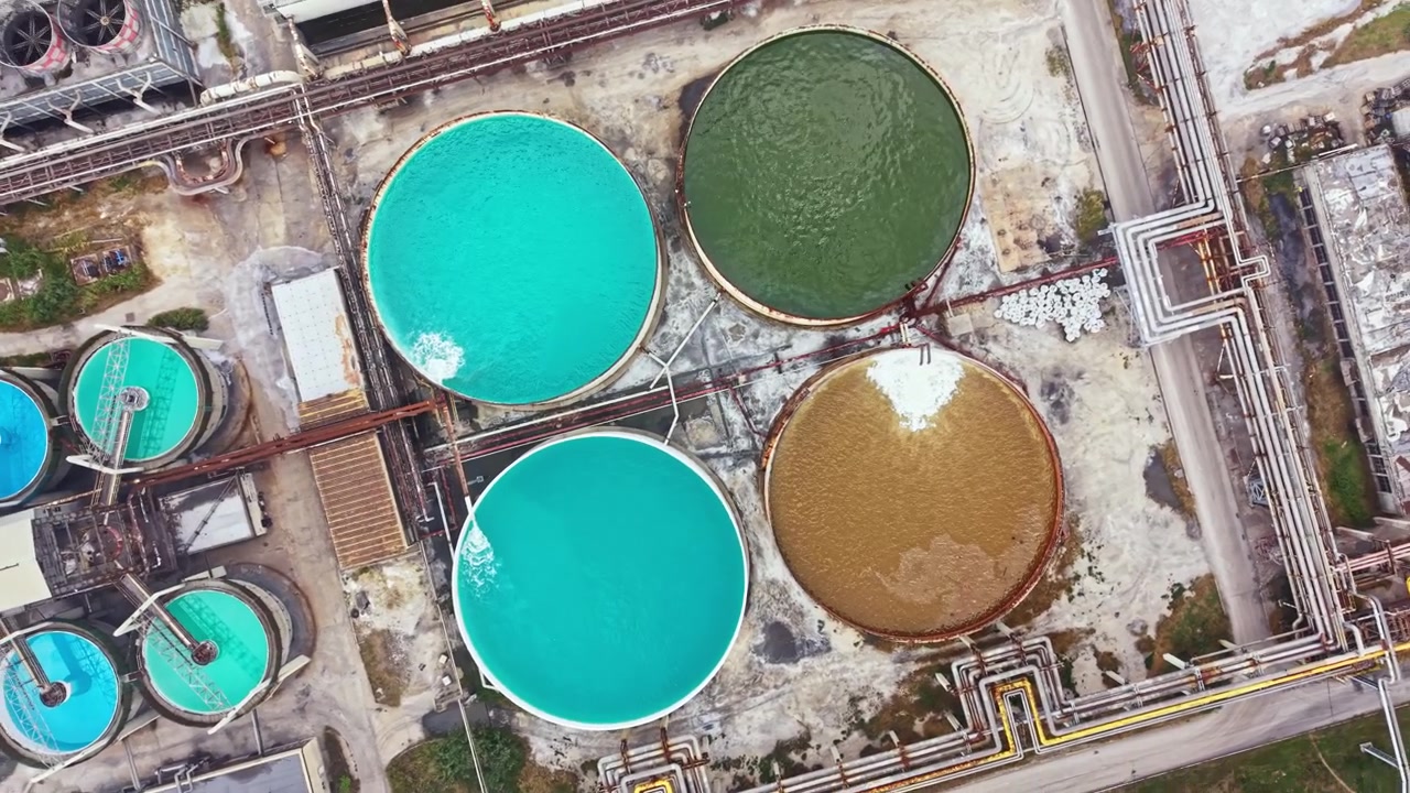 Bright colored tanks sit at a factory near a road showing different colors of liquids held inside them during daylight