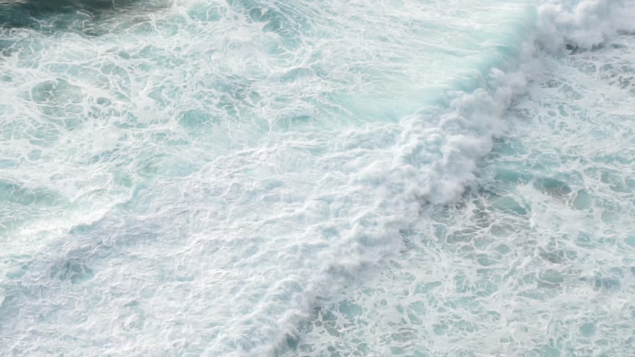 Vue aérienne de vagues océaniques blanches s'écrasant sur une côte rocheuse noire depuis une falaise, Bali, Indonésie