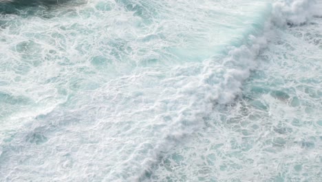 view of white ocean waves crashing into black rocky shore from above off of a cliff, bali, indonesia