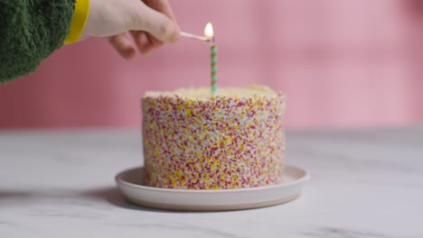 studio shot birthday cake covered with decorations and single candle being lit 4