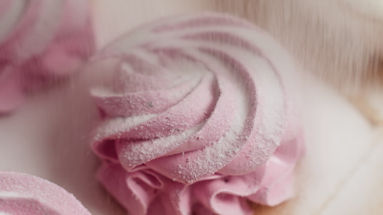 Extreme close up of sugar being gently sprinkled on swirl pink cupcake showcasing fine texture of frosting and sugar granules, highlighting dessert elegant detail and pastel color
