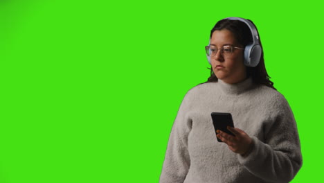 Young-Woman-Wearing-Wireless-Headphones-Streaming-Music-From-Mobile-Phone-Against-Studio-Green-Screen-1