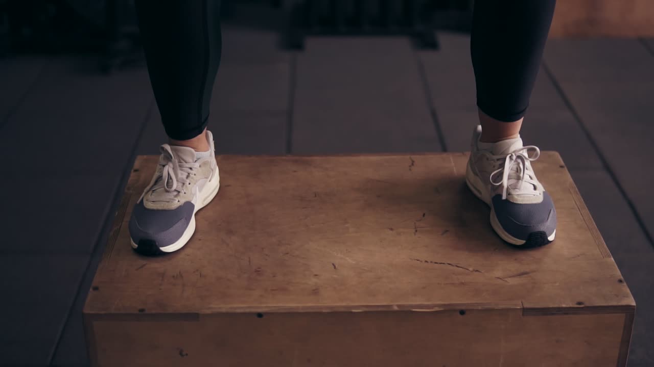 perspectiva de la parte inferior del entrenador deportivo femenino saltando en una plataforma de madera en el gimnasio.