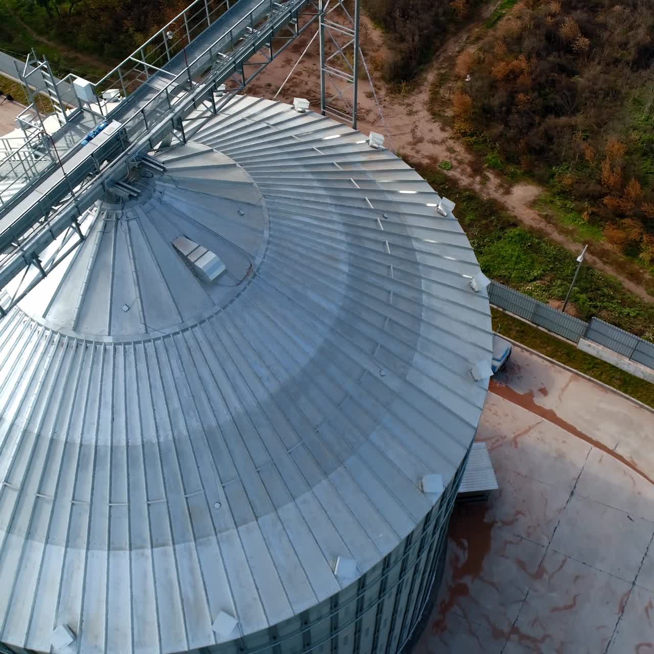 Large storage tank. Modern metal grain elevator on field. Granary for storing and processing agricultural crop. Aerial view.
