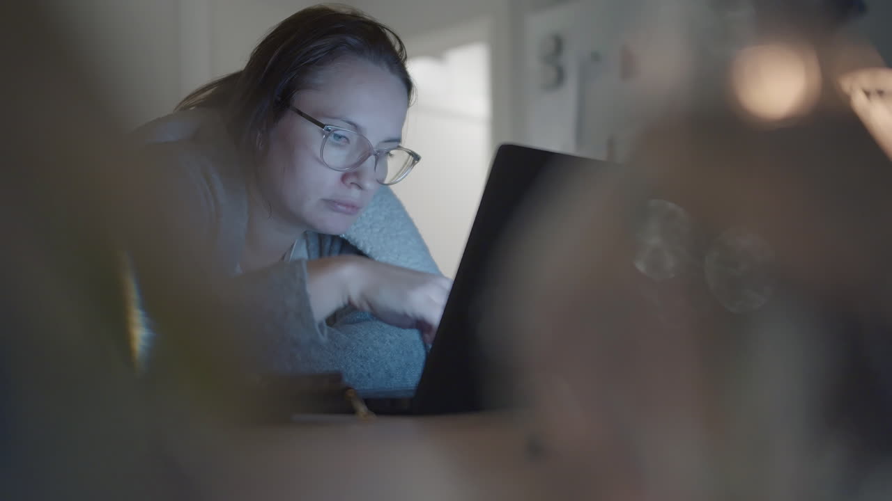 mujer con gafas y trabajando en línea cerca de una laptop en un entorno doméstico