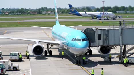 a large airplane is getting ready for its upcoming flight as ground crew members assist with loading and preparations. various planes can be seen taking off and taxiing around the airport.