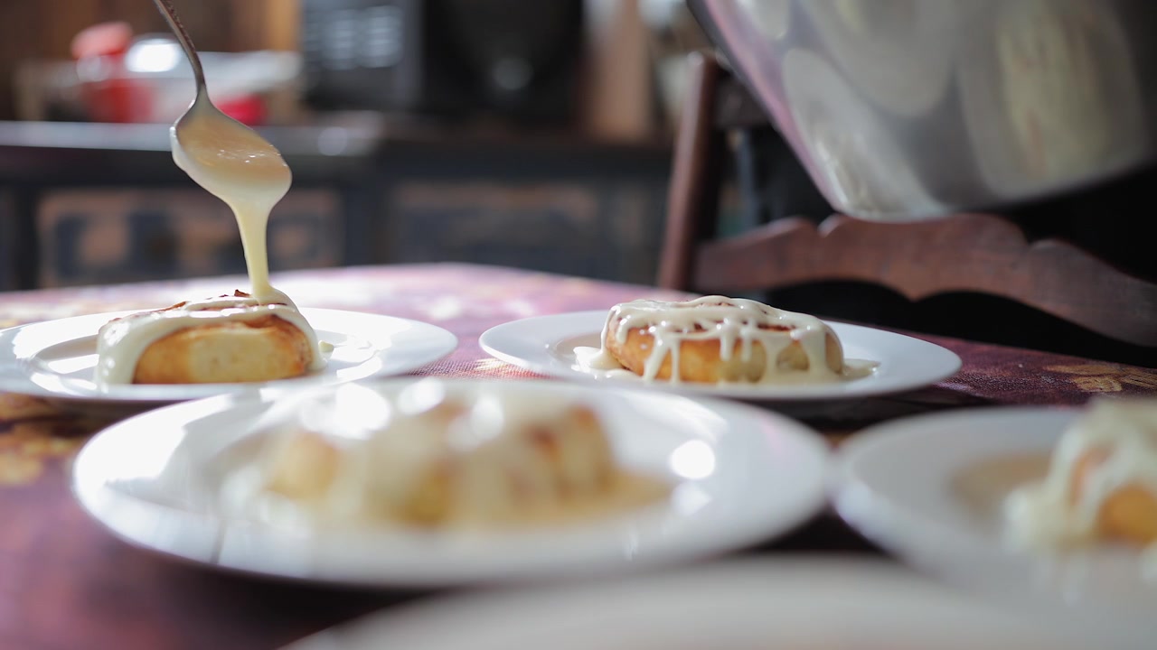 Low angle view: Icing is drizzled onto cinnamon buns in kitchen plates