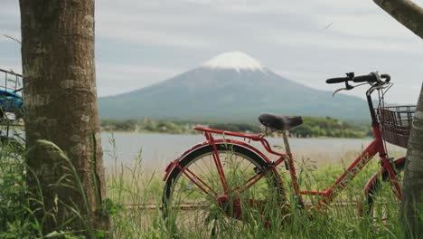 reveal shot overlooking kawaguchi lake with the majestic mt. fuji in the background, and red bicycle in the foreground under bright sunny sky in japan.