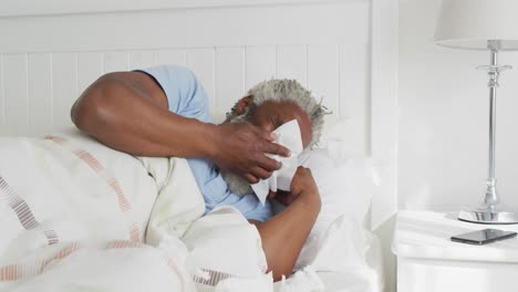 senior man with tissue sneezing in the bed at home