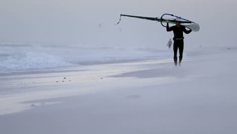 Male-surfer-carrying-windsurfer-in-the-beach-4k