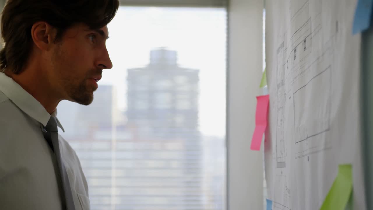 vista lateral de un joven ejecutivo caucásico que trabaja en un plano en un tablero de vidrio en una oficina moderna 4k