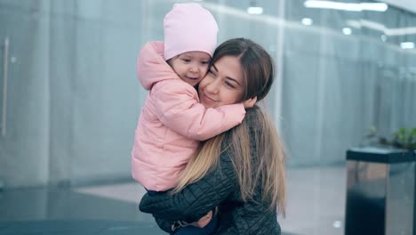 Cu-4k-Joven-Y-Hermosa-Madre-Abraza-A-Una-Pequeña-Hija,-Están-En-Un-Centro-De-Negocios-Sonriendo