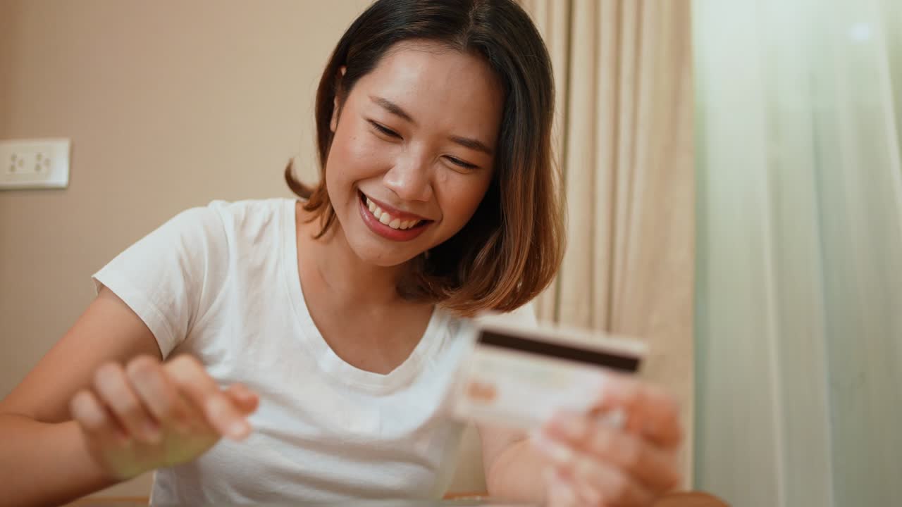 慢动作：亚洲女性在家中用笔记本电脑在电商网站上选择折扣商品，手持信用卡，体现在线购物支付概念
