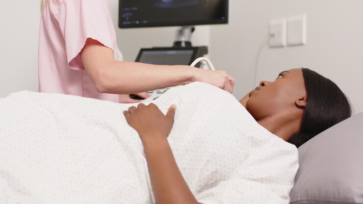 Paziente afroamericana con infermiera in rosa che posiziona e fa scorrere la sonda per la scansione in clinica