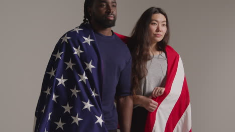 retrato de estudio de una pareja multicultural envuelta en la bandera estadounidense celebrando el día de la independencia del 4 de julio