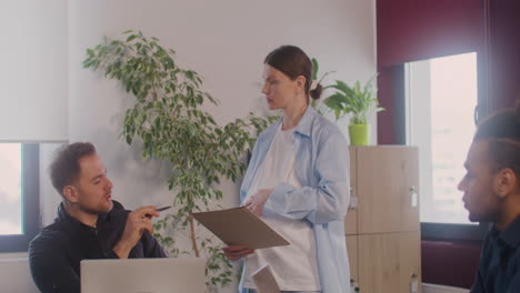 pregnant woman is explaining a project talking with a coworker in a meeting room while she is touching her belly