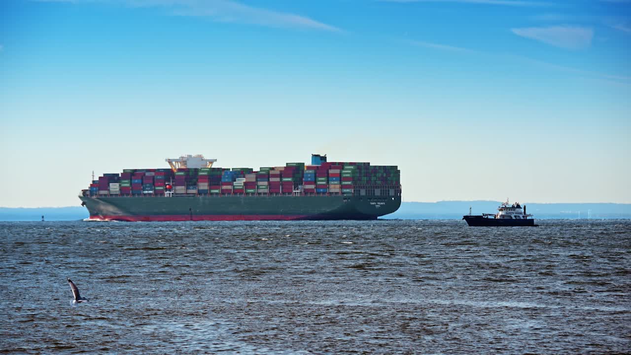 New York, USA, 5 October 2025: Large green cargo ship accompanied by a safety vessel. Massive container vessel sailing on open water with a small pilot or safety boat nearby