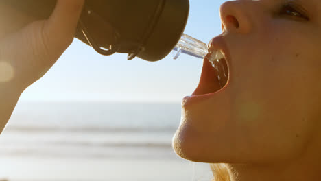 Mujer-En-Forma-Bebiendo-Agua-En-La-Playa-4k