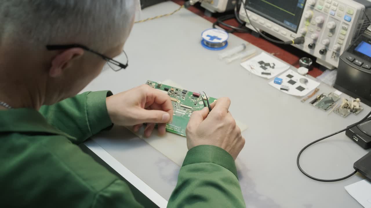 Electronic equipment repair shop. The Engineer Technician solders the printed circuit board of an electronic device under a microscope.