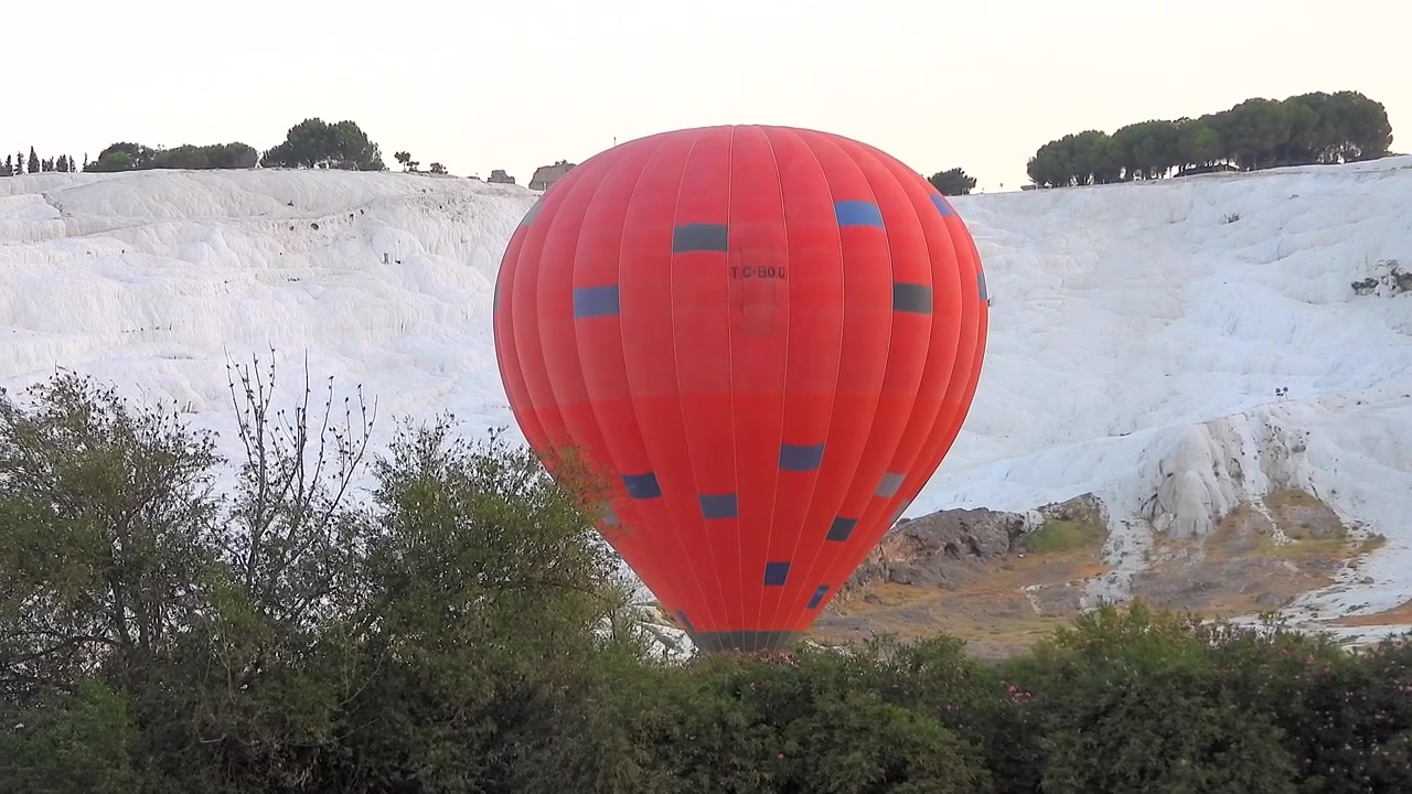 Balão de ar quente vermelho flutuando sobre os Travertinos de Pamukkale