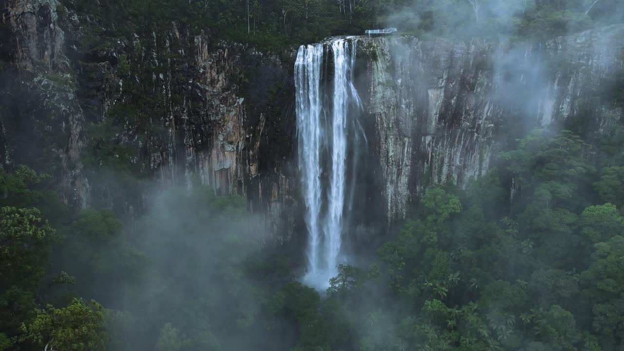 vista única de drones a través de una niebla suspendida que revela una majestuosa cascada que se derrama sobre un exuberante paisaje montañoso de selva tropical