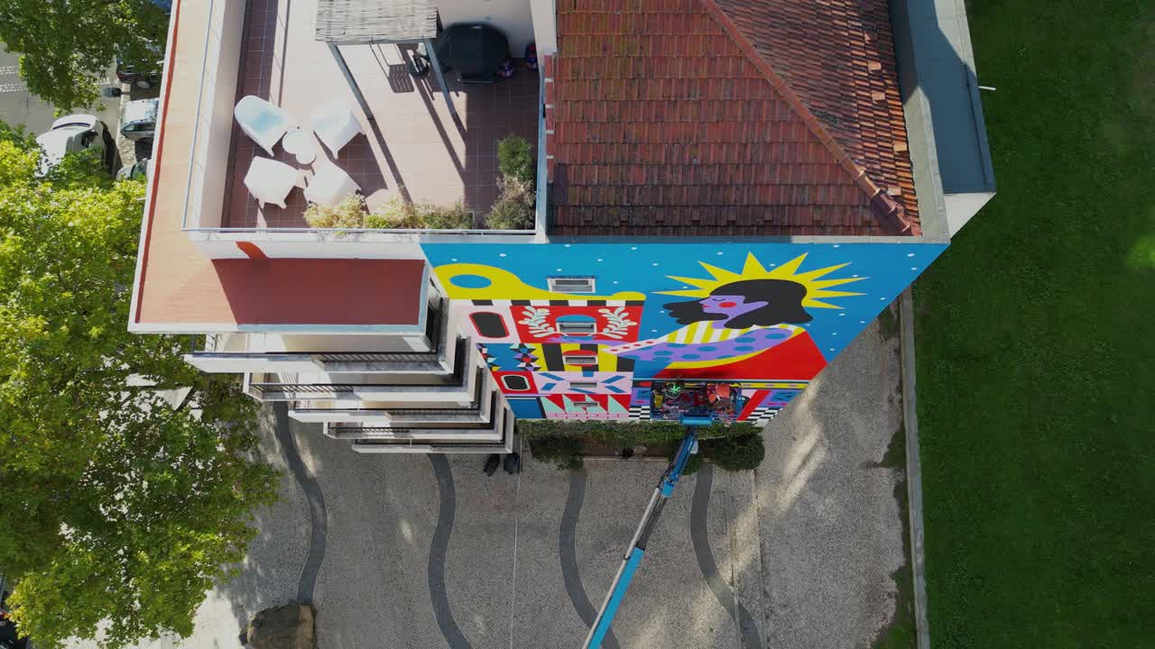 Aerial view of Lisbon: A high-angle shot captures an artist and others painting a vibrant mural on a building, infusing creative energy into the city's urban landscape