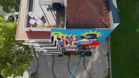 Aerial view of Lisbon: A high-angle shot captures an artist and others painting a vibrant mural on a building, infusing creative energy into the city&#039;s urban landscape