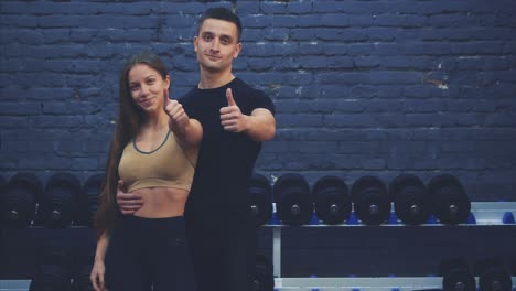 una hermosa joven y su bien construido novio juntos muestran una clase de gestos. se alegran de verse el uno al otro en el gimnasio.