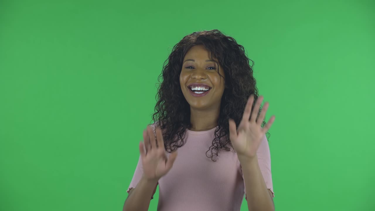 retrato de una hermosa joven afroamericana está mirando a la cámara y avergonzada. morena ardiente con cabello ondulado en vaqueros y una blusa beige en una pantalla verde en el estudio