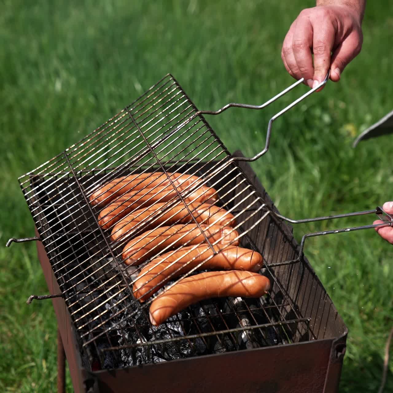 Sausages roasting on barbecue grill outdoors. Grilled food fried and smoked in charcoal grills. Man chef putting delicious sausages on a grill grate. Food for picnic