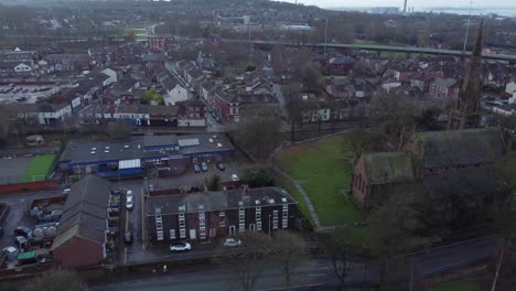 Gloomy-early-morning-riverside-church-with-spire-aerial-view-across-industrial-British-North-West-town-residence-roofing-dolly-left