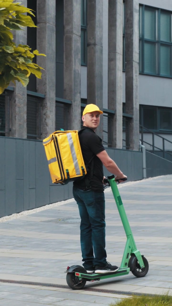 A delivery person rides a scooter carrying a yellow insulated bag for food delivery captured in a