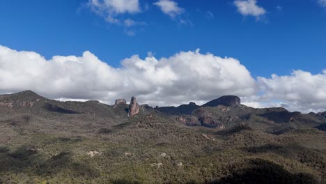 drone camera smoothly pans across rugged volcanic peaks and forested hills under bright daylight, revealing dramatic clouds and expansive australian wilderness