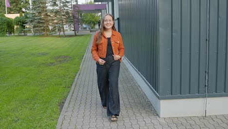 playful brunette cute woman in black jumper orange jacket walks smiling with joy in urban setting