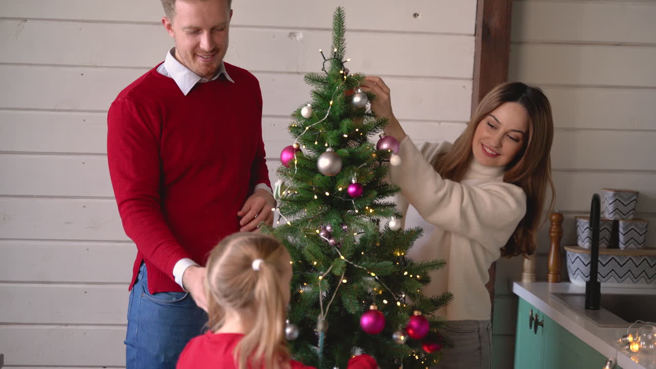pareja feliz y su hija colgando decoración navideña en el árbol de navidad en casa 1