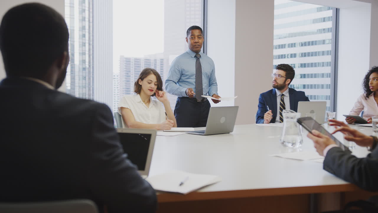 hombre de negocios maduro de pie dando una presentación a sus colegas sentados alrededor de la mesa en una oficina moderna